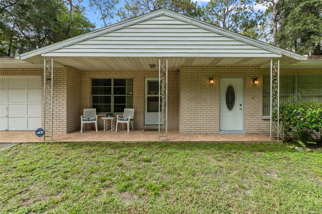 A single-story brick house features a covered front porch with decorative metal columns and chairs — 6095 ZIRKELS CIRCLE, BROOKSVILLE, FL