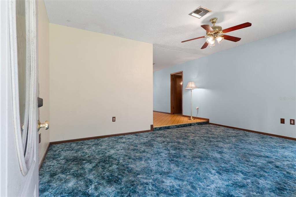 A room with blue carpet, light-colored walls, a ceiling fan, and a raised hallway entrance — 6095 ZIRKELS CIRCLE, BROOKSVILLE, FL