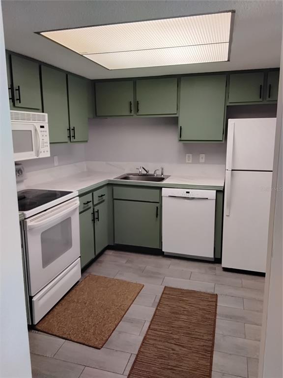 A kitchen features sage green cabinets, white appliances, a stainless steel sink, and tile flooring — 570 BAHIA CIRCLE UNIT B, OCALA, FL