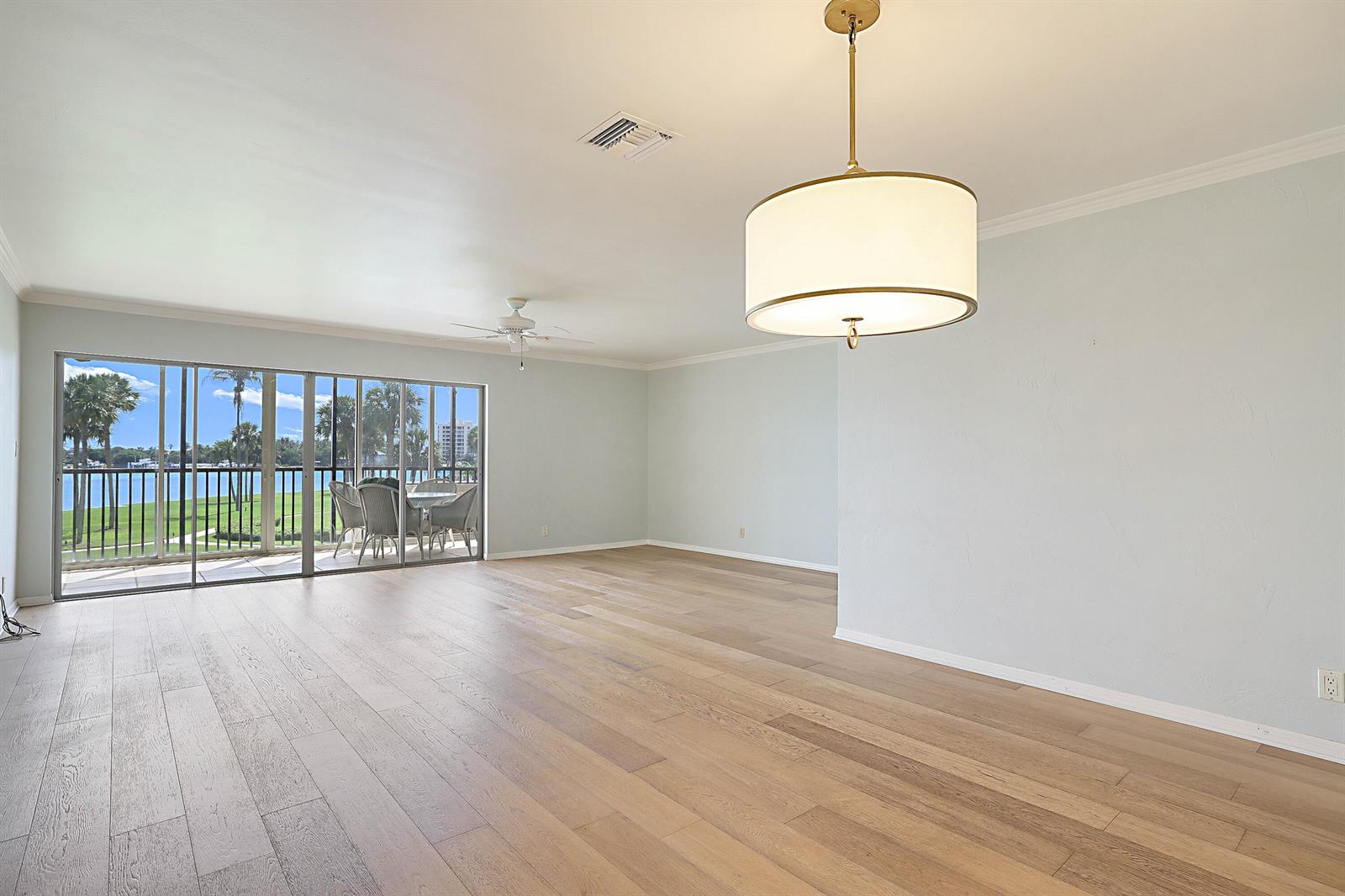 An empty living room with light wood flooring, a drum pendant light, and sliding glass doors — 300 Intracoastal Place # 204, Jupiter FL 33469, JUPITER, FL