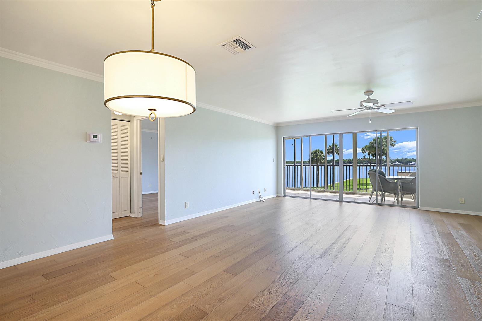 An empty living room with light wood floors, a drum pendant light, and a balcony view — 300 Intracoastal Place # 204, Jupiter FL 33469, JUPITER, FL
