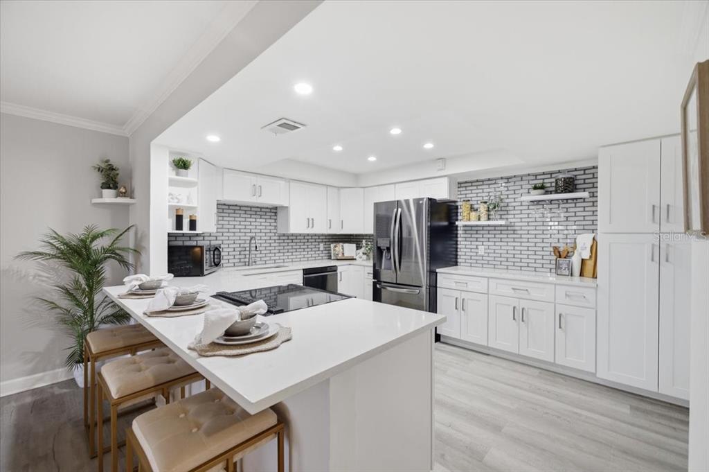 A modern white kitchen features a breakfast bar, stainless steel appliances, and gray subway tile — 4908 38TH WAY S UNIT 401, ST PETERSBURG, FL