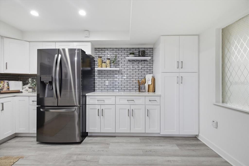 A modern kitchen features white cabinets, a dark stainless steel refrigerator, and a gray-tiled backsplash — 4908 38TH WAY S UNIT 401, ST PETERSBURG, FL