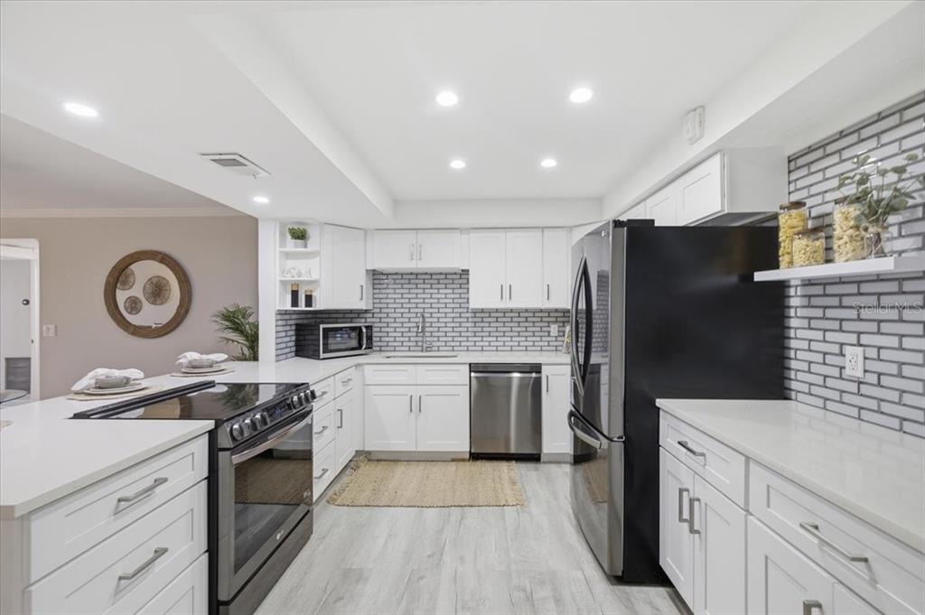 A modern kitchen features white cabinets, stainless steel appliances, and a gray brick backsplash — 4908 38TH WAY S UNIT 401, ST PETERSBURG, FL