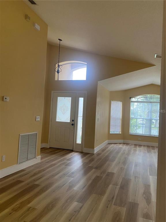 An entryway with high ceilings, light-colored walls, and wood-look flooring leads to a front door — 10007 DORIATH CIRCLE, ORLANDO, FL
