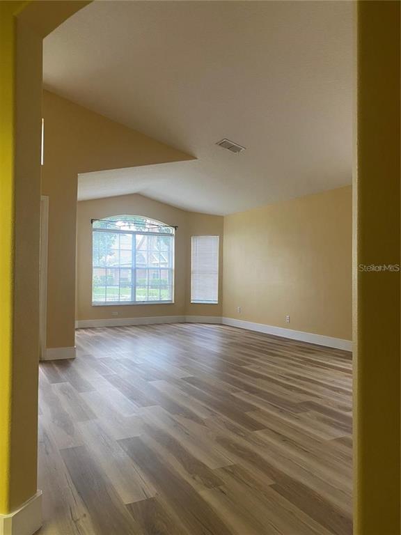 An empty living room features light wood-look flooring, vaulted ceilings, and a large arched window — 10007 DORIATH CIRCLE, ORLANDO, FL