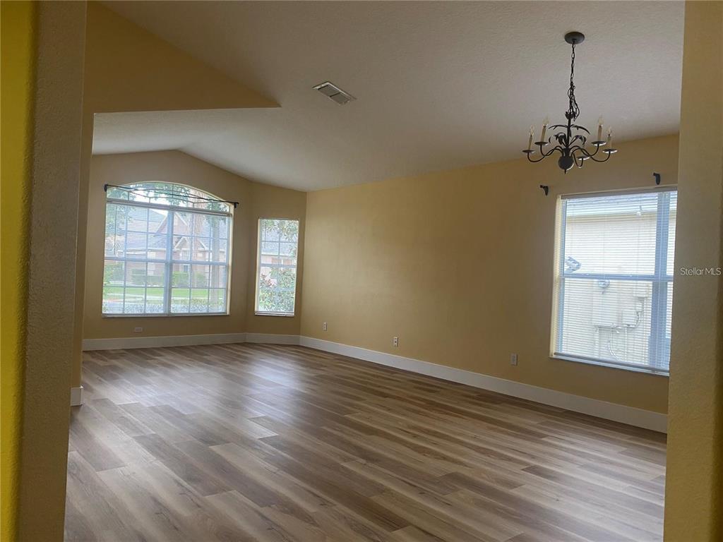 An empty living room features light-colored walls, wood-look flooring, a chandelier, and large windows — 10007 DORIATH CIRCLE, ORLANDO, FL