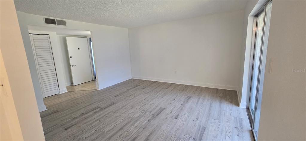 An empty living room features light-colored wood-look flooring, white walls, and a sliding glass door — 375 S MCMULLEN BOOTH ROAD UNIT 95, CLEARWATER, FL