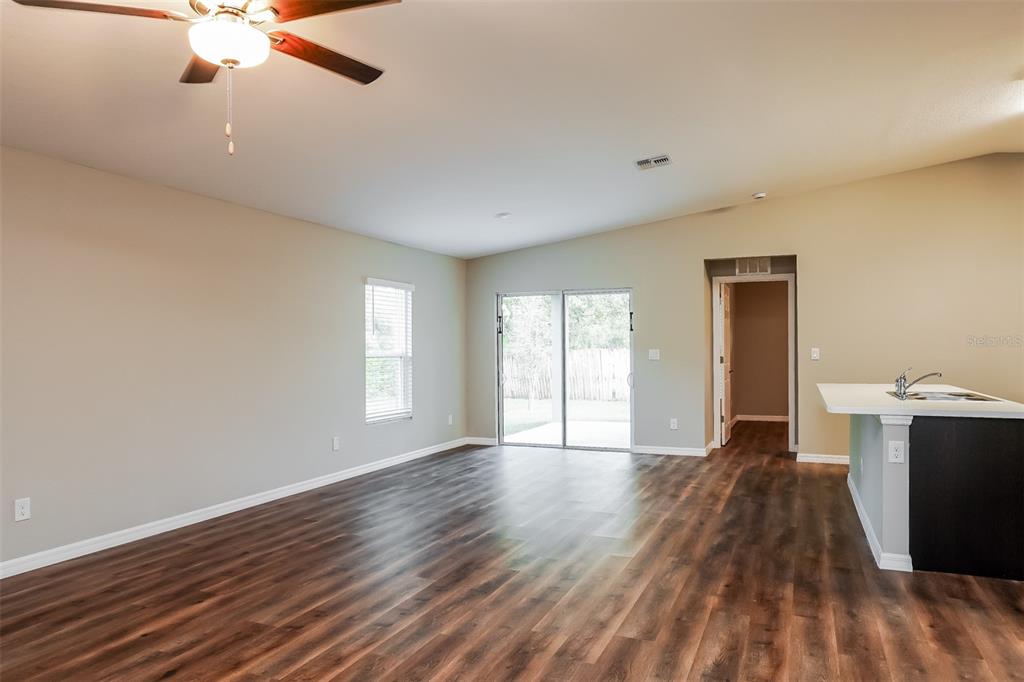 An open-concept living area features dark wood-look flooring, a ceiling fan, and sliding glass doors — 4638 JASLO AVENUE, NORTH PORT, FL