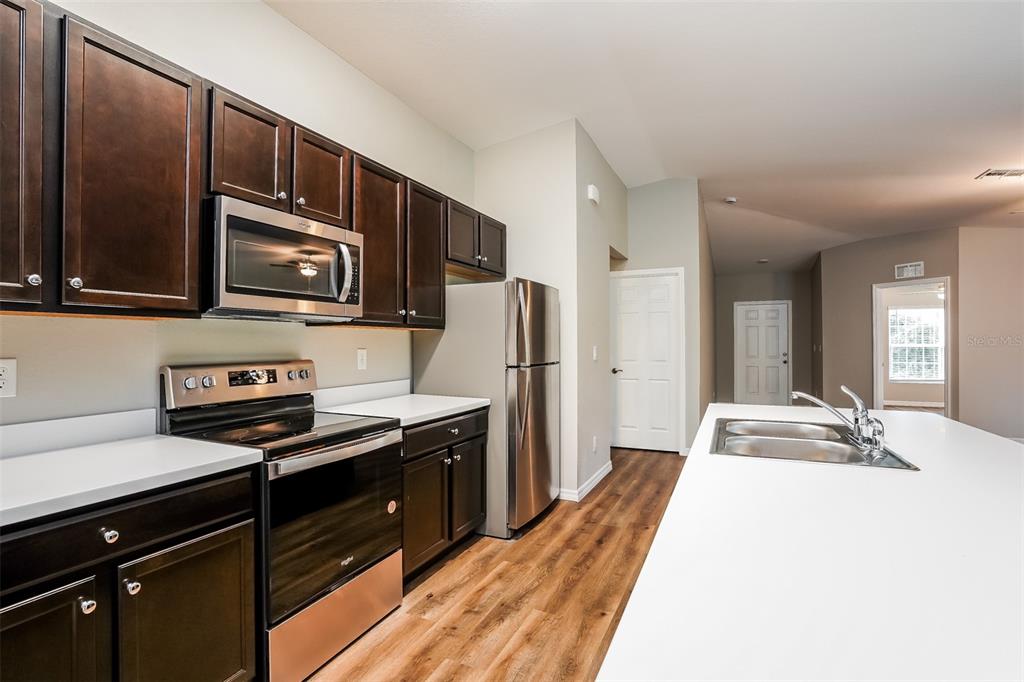 A kitchen features dark wood cabinets, stainless steel appliances, white countertops, and wood-look flooring — 4638 JASLO AVENUE, NORTH PORT, FL