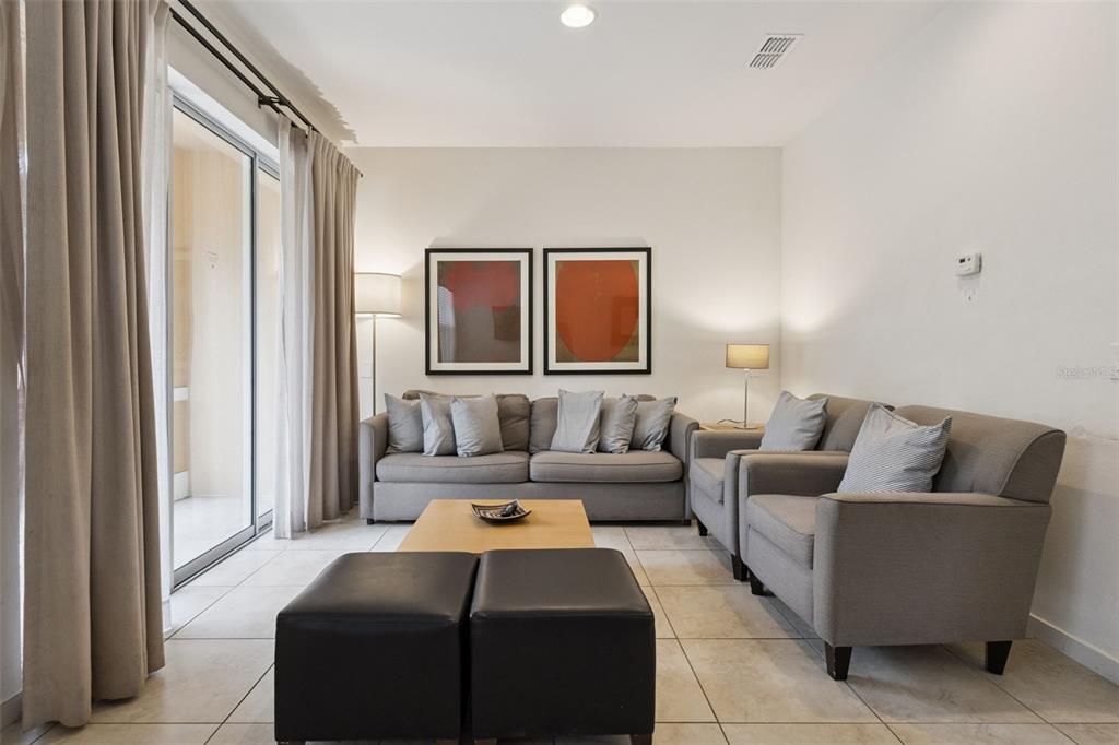 A living room features a grey sofa, matching armchairs, two black ottomans, and sliding glass doors — 2711 COUPE STREET, KISSIMMEE, FL