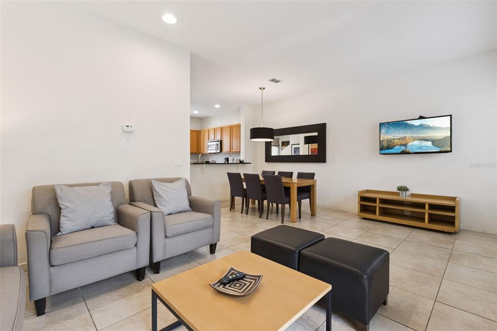 An open-concept living and dining area features tile floors, neutral walls, and a mounted television — 2711 COUPE STREET, KISSIMMEE, FL