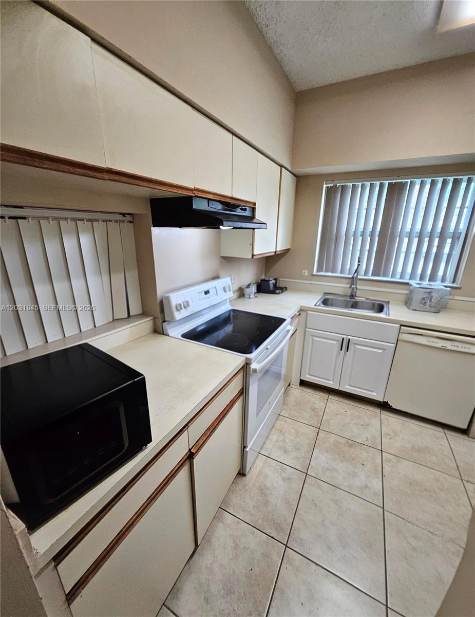 A kitchen features beige cabinets, white appliances, a tiled floor, and a window with blinds — 631 Cypress Lake Blvd # E17, Deerfield Beach FL 33064, DEERFIELD BEACH, FL