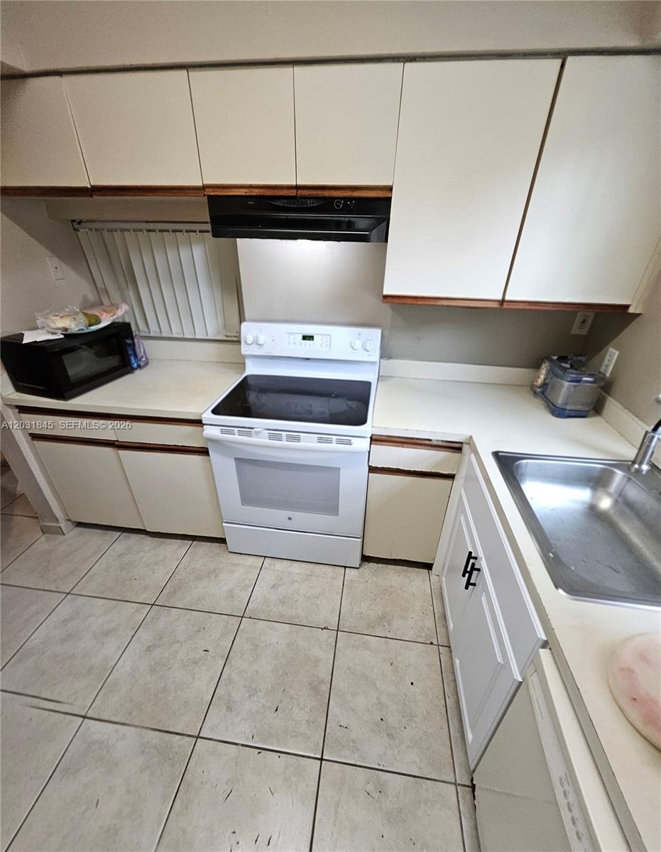 A kitchen features white cabinets, a black microwave, a white electric stove, and tiled floors — 631 Cypress Lake Blvd # E17, Deerfield Beach FL 33064, DEERFIELD BEACH, FL