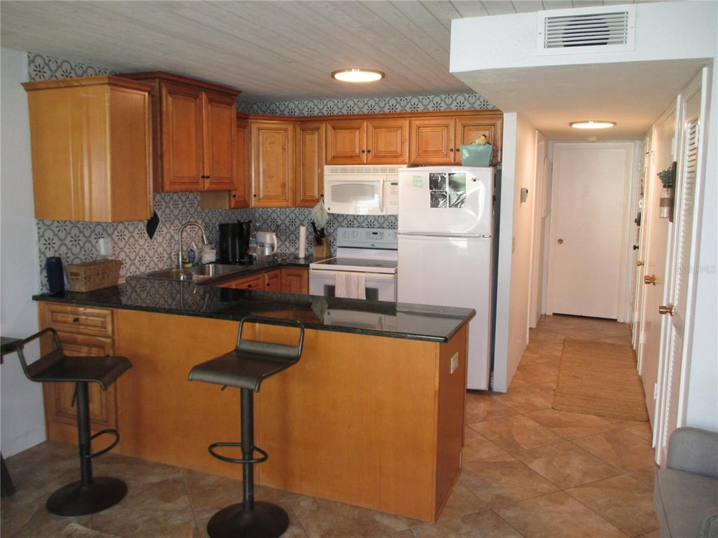 A kitchen features wood cabinets, dark granite countertops, a breakfast bar, and tile flooring — 1441 N ATLANTIC AVENUE UNIT 113, DAYTONA BEACH, FL