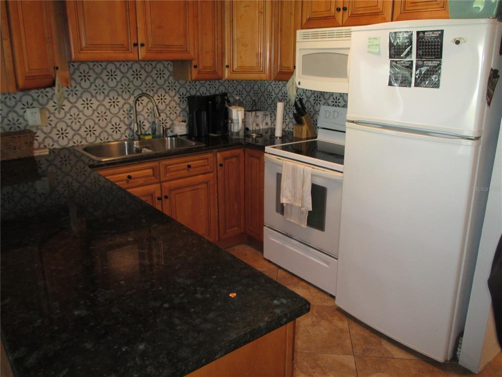 A kitchen features wood cabinets, dark granite countertops, a patterned backsplash, and white appliances — 1441 N ATLANTIC AVENUE UNIT 113, DAYTONA BEACH, FL