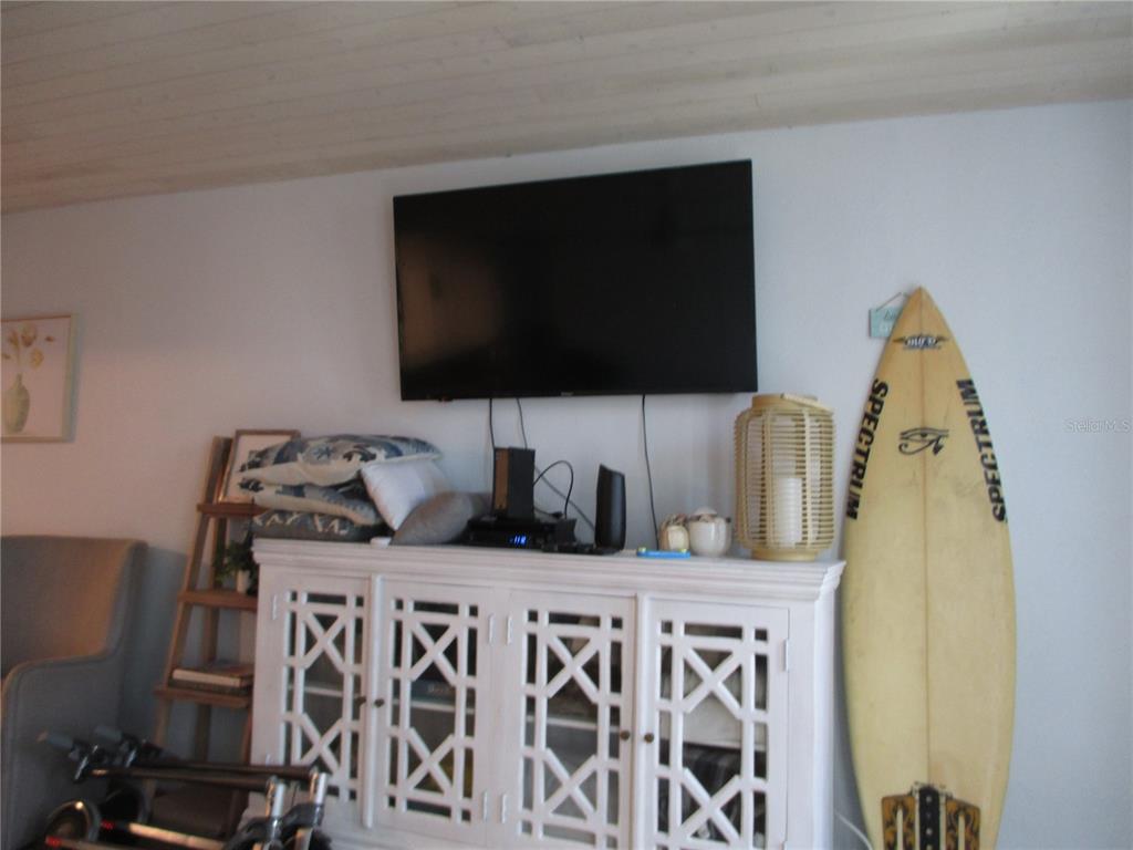 A white media console sits beneath a wall-mounted television with a surfboard nearby — 1441 N ATLANTIC AVENUE UNIT 113, DAYTONA BEACH, FL