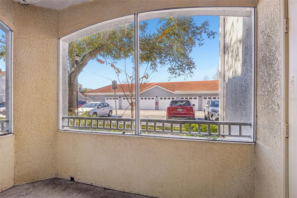 A screened-in porch with textured walls looks out toward a parking area and garage building — 18001 RICHMOND PLACE DRIVE UNIT 1213, TAMPA, FL