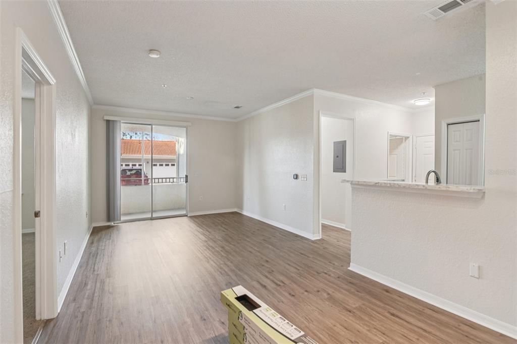 An open-concept living area features wood-look flooring, a sliding glass door, and a kitchen pass-through — 18001 RICHMOND PLACE DRIVE UNIT 1213, TAMPA, FL