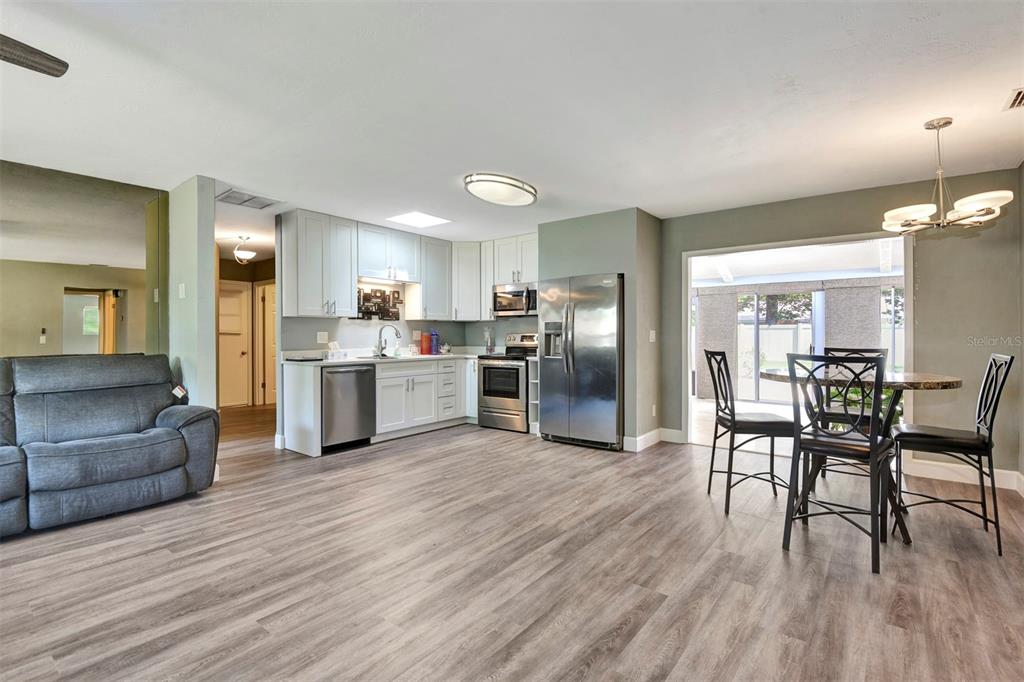 An open-concept kitchen and dining area features white cabinets, stainless steel appliances, and wood-look flooring — 781 LITTLE PINE DRIVE, SOUTH DAYTONA, FL