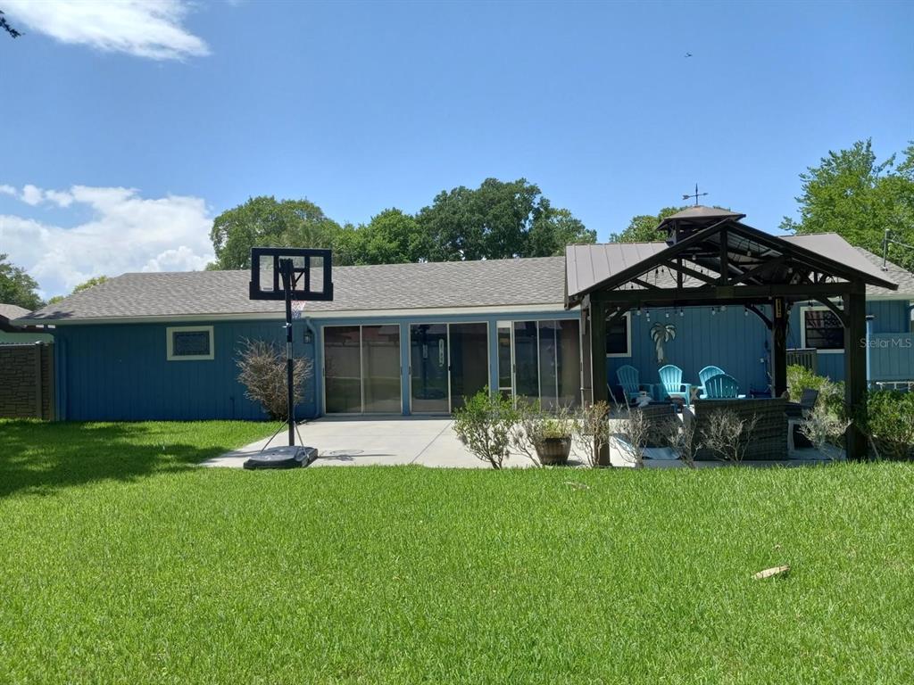 A blue house exterior features a concrete patio, a basketball hoop, and a wooden gazebo — 781 LITTLE PINE DRIVE, SOUTH DAYTONA, FL