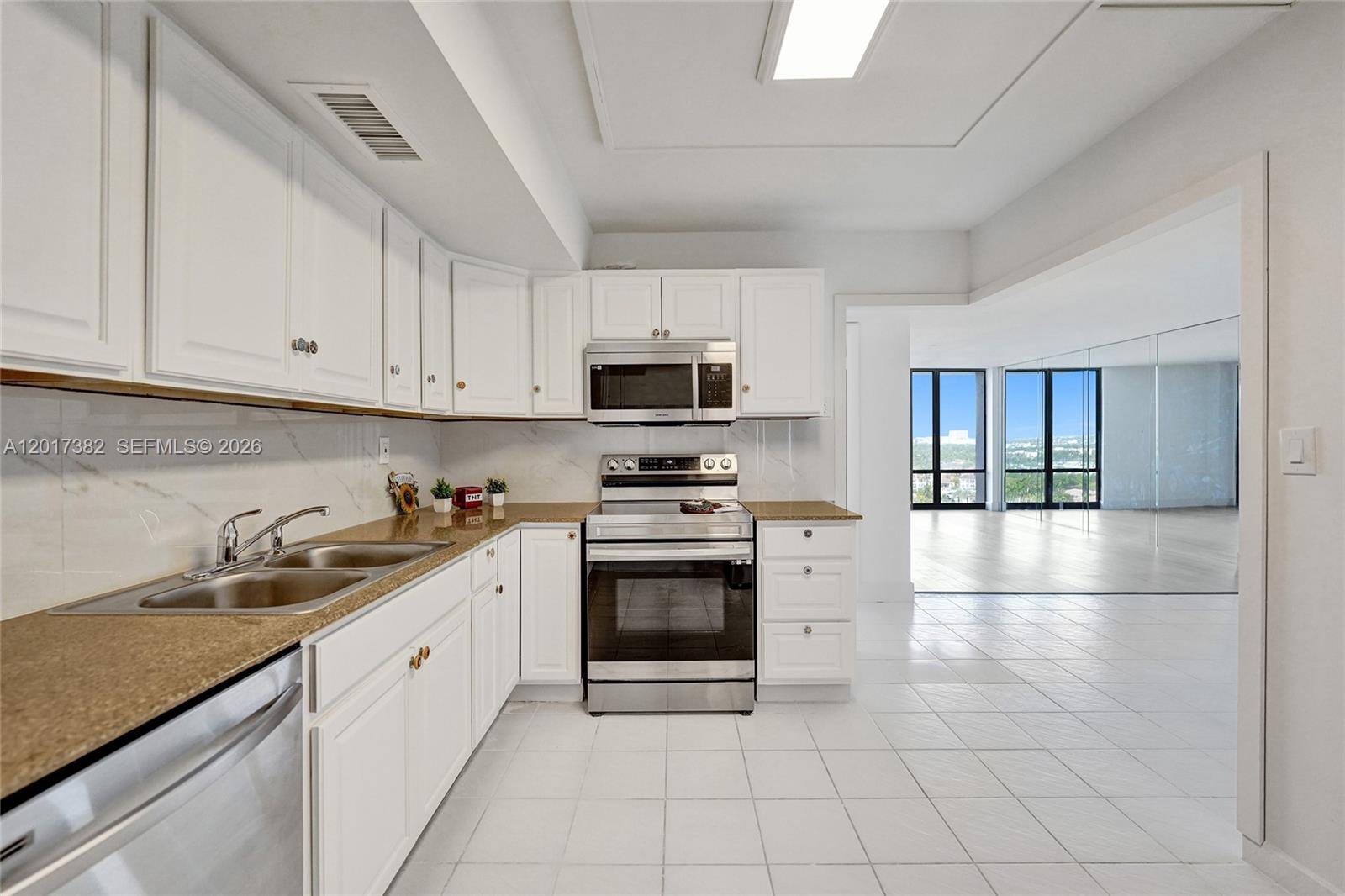 A kitchen with white cabinets, stainless steel appliances, and tile flooring opens to a living area — 1600 S Ocean Dr # 16B, Hollywood FL 33019, HOLLYWOOD, FL