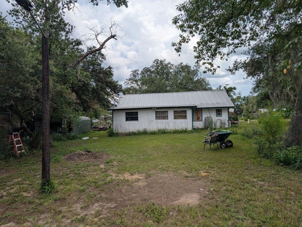 A white, single-story house with a metal roof sits in a grassy, tree-filled yard — 20877 SE 143RD PLACE, UMATILLA, FL