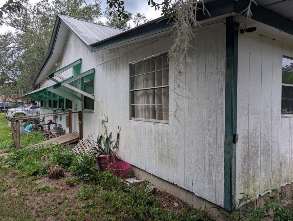 The exterior of a white house features a metal roof, green trim, and a wooden ramp — 20877 SE 143RD PLACE, UMATILLA, FL