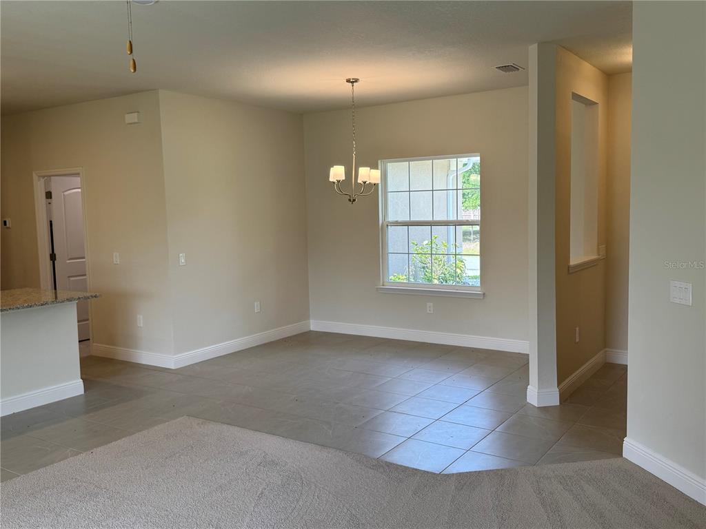 A dining area with tile flooring, a chandelier, and a window, adjacent to a carpeted room — 5874 FERENDINA STREET, NORTH PORT, FL