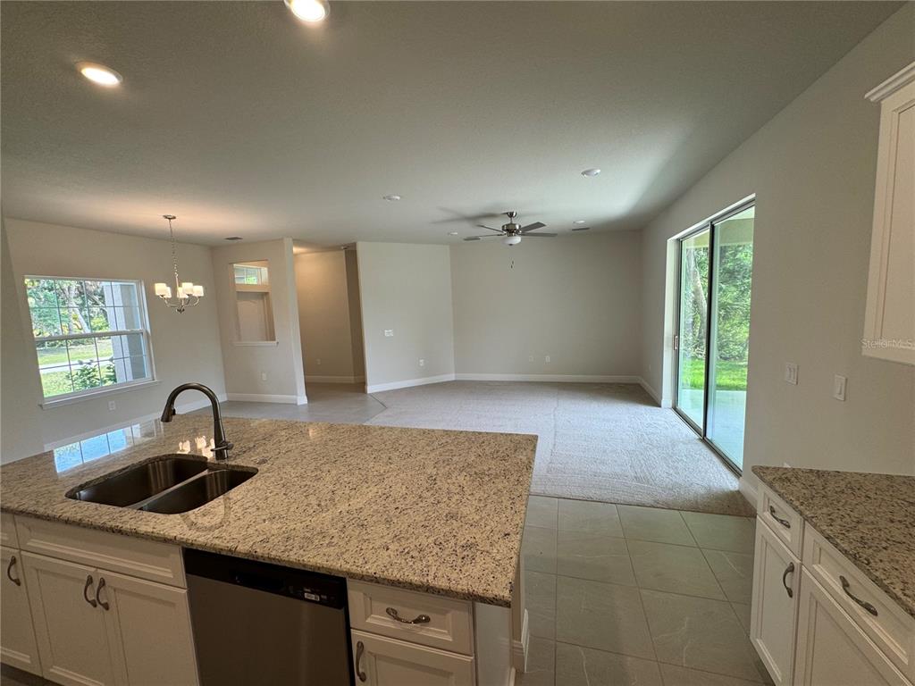 A kitchen island with a granite countertop overlooks an open-concept living area with carpeted flooring — 5874 FERENDINA STREET, NORTH PORT, FL