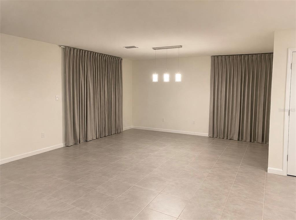 An empty room with light-colored tile flooring, beige walls, and floor-to-ceiling gray curtains — 35348 SPRUCE KNOB COURT, DADE CITY, FL