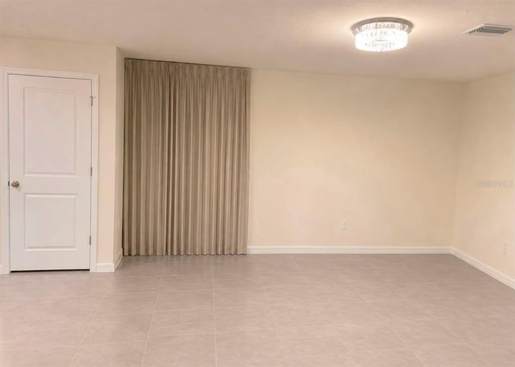 An empty room features light-colored tile flooring, a white door, and floor-to-ceiling beige curtains — 35348 SPRUCE KNOB COURT, DADE CITY, FL