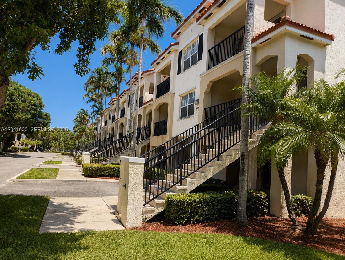 Exterior view of a multi-story apartment building with outdoor staircases and palm trees — 5980 W Sample Rd # 308, Coral Springs FL 33067, CORAL SPRINGS, FL