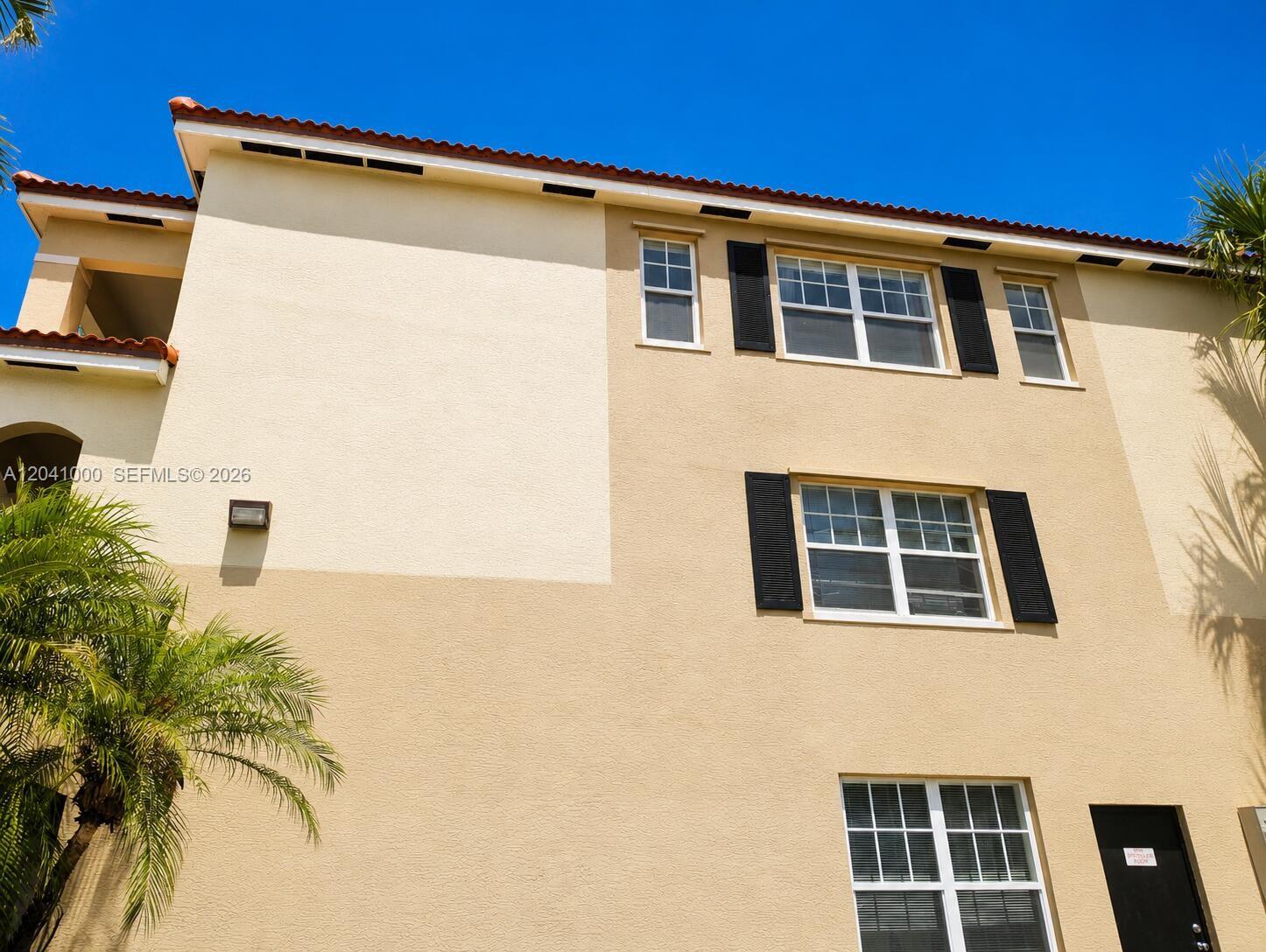 A low-angle view of a multi-story tan stucco building with a red tile roof — 5980 W Sample Rd # 308, Coral Springs FL 33067, CORAL SPRINGS, FL