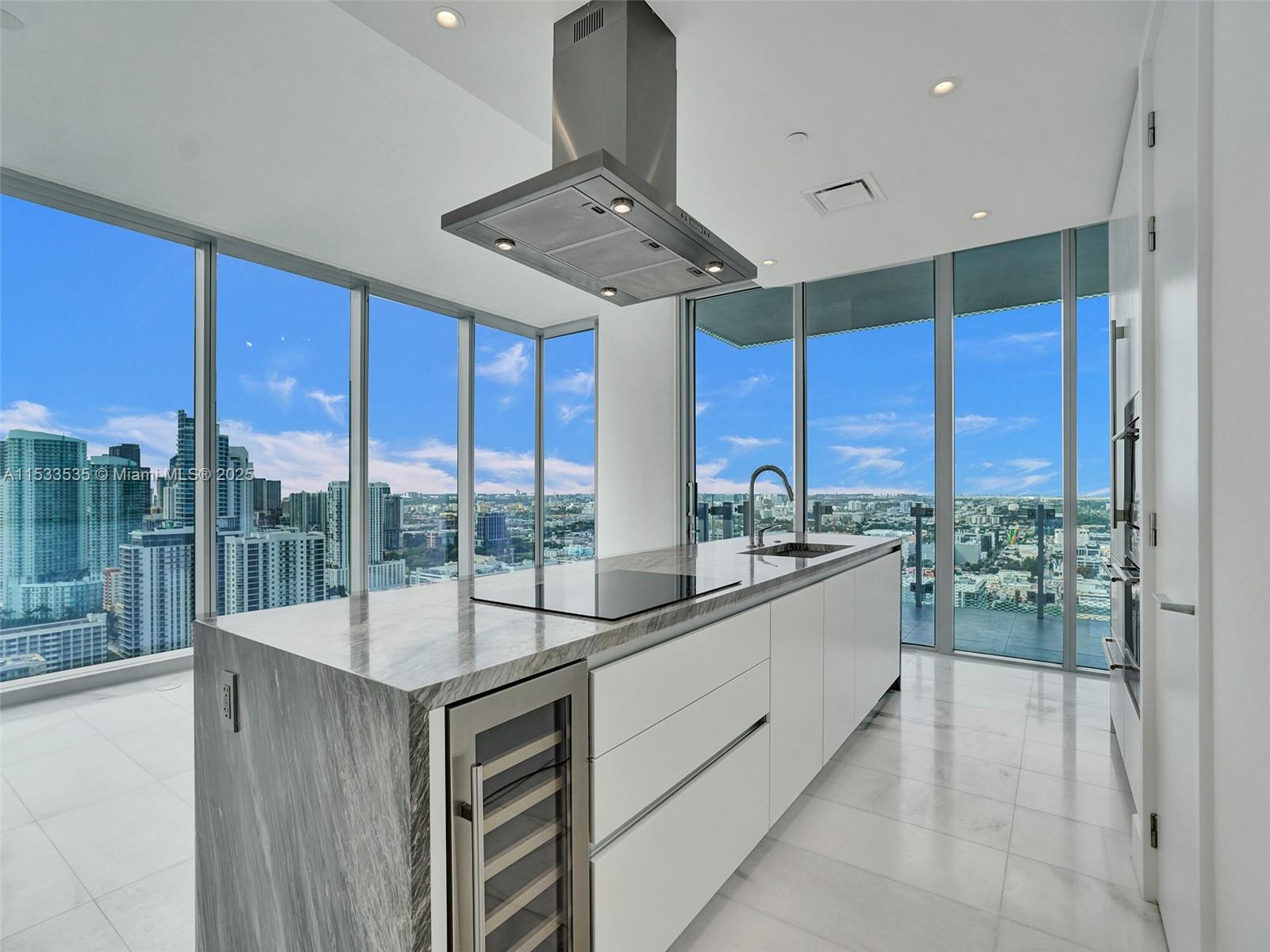 A modern kitchen island with a marble countertop and wine cooler overlooks a city skyline — 700 NE 26th Ter # 3505, Miami FL 33137, MIAMI, FL