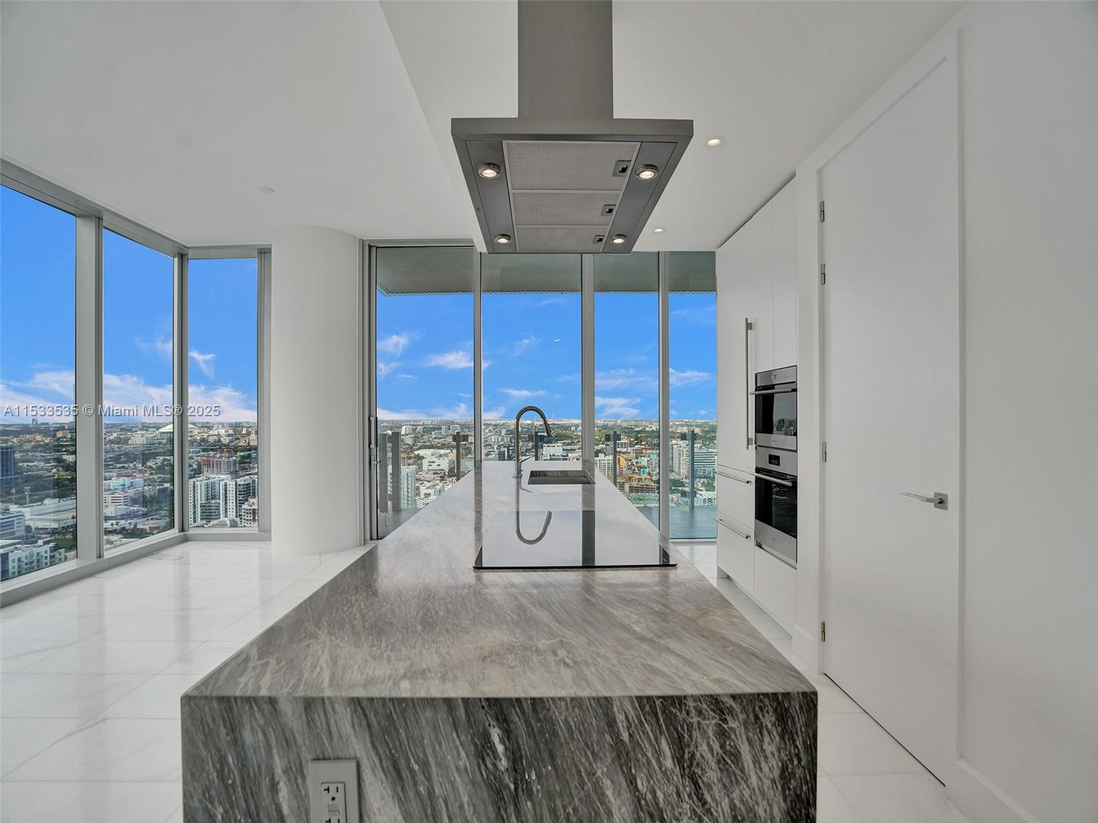A modern kitchen features a large stone island, white cabinetry, and floor-to-ceiling windows with city views — 700 NE 26th Ter # 3505, Miami FL 33137, MIAMI, FL