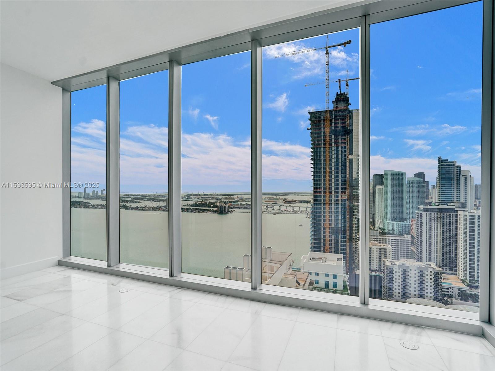 A minimalist room with white marble floors features floor-to-ceiling windows overlooking a city skyline — 700 NE 26th Ter # 3505, Miami FL 33137, MIAMI, FL