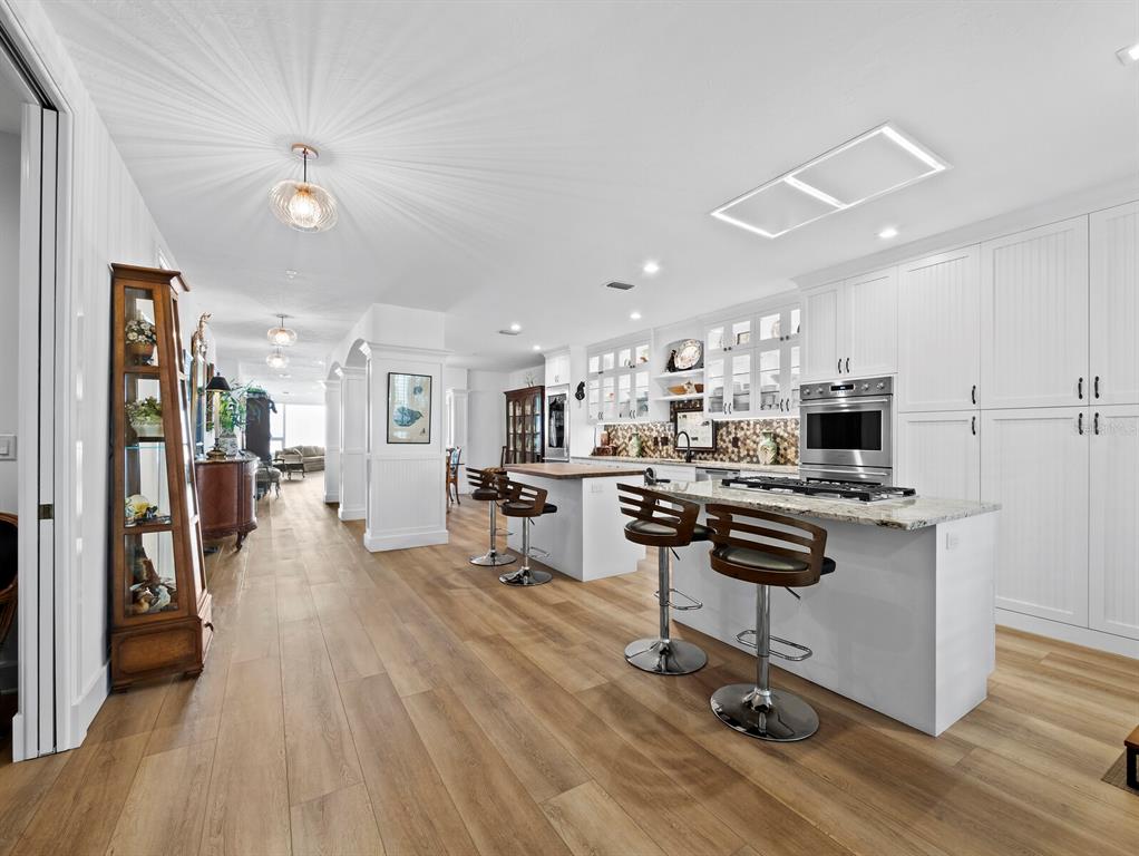 A modern kitchen features white cabinetry, a granite-topped island with bar stools, and wood flooring — 340 GULF OF MEXICO DRIVE UNIT 112, LONGBOAT KEY, FL
