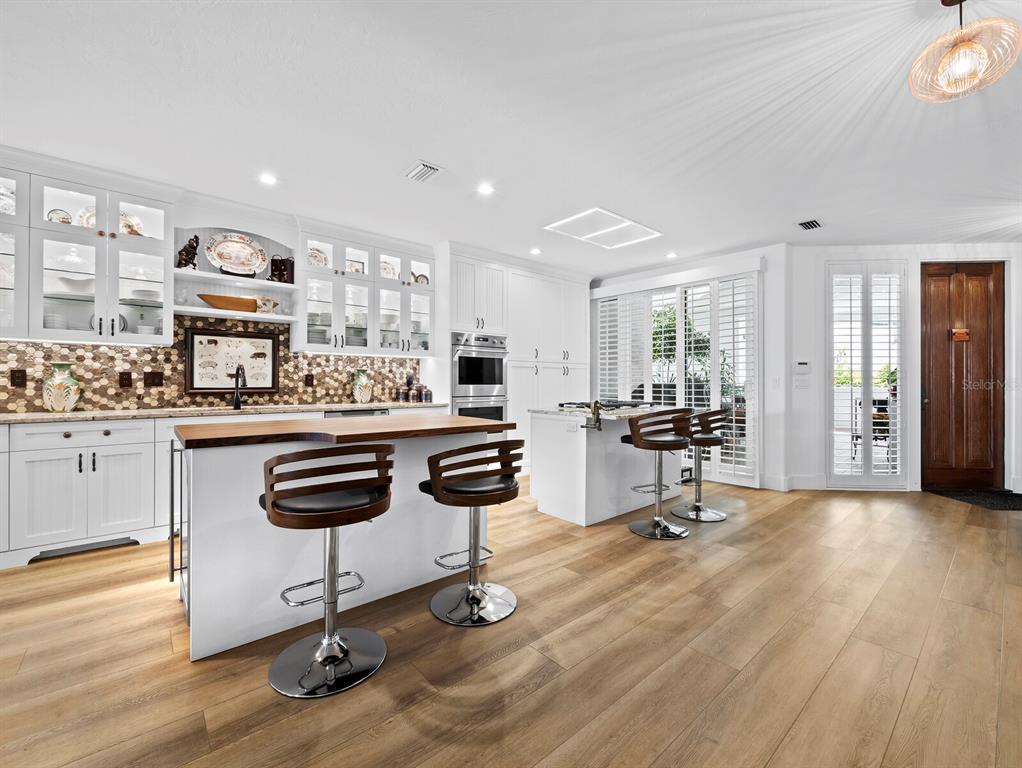 A bright kitchen features white cabinetry, two islands with bar stools, and wood-look flooring — 340 GULF OF MEXICO DRIVE UNIT 112, LONGBOAT KEY, FL