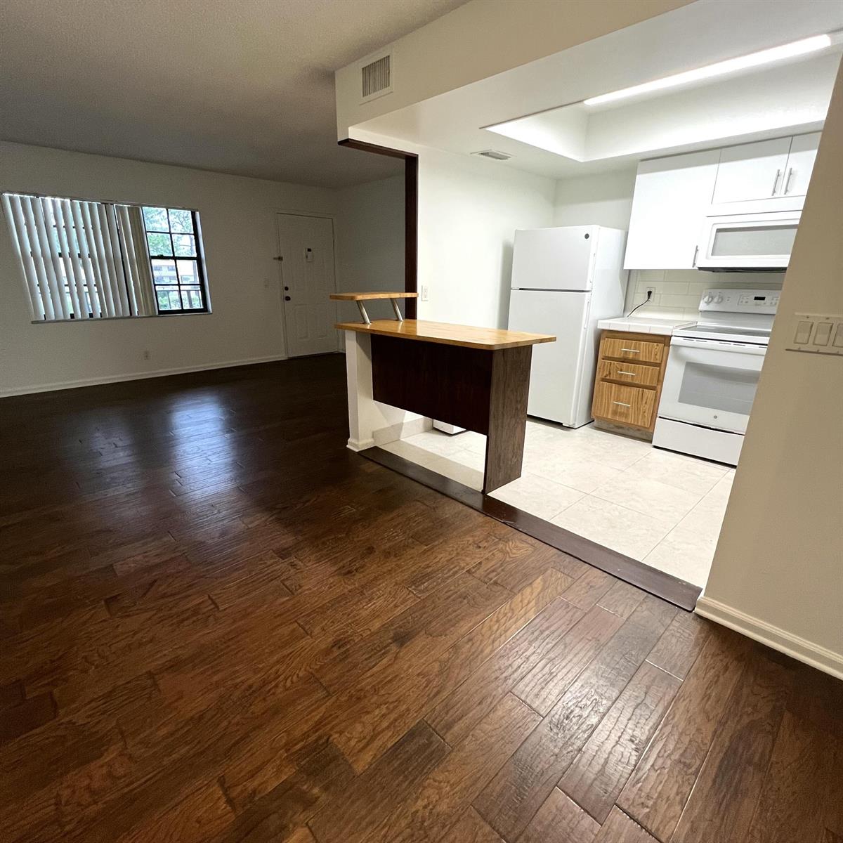 A kitchen with white appliances and wood cabinets opens into a living area with flooring — 4205 Oak Terrace Drive # 4205, FL 33463, FL