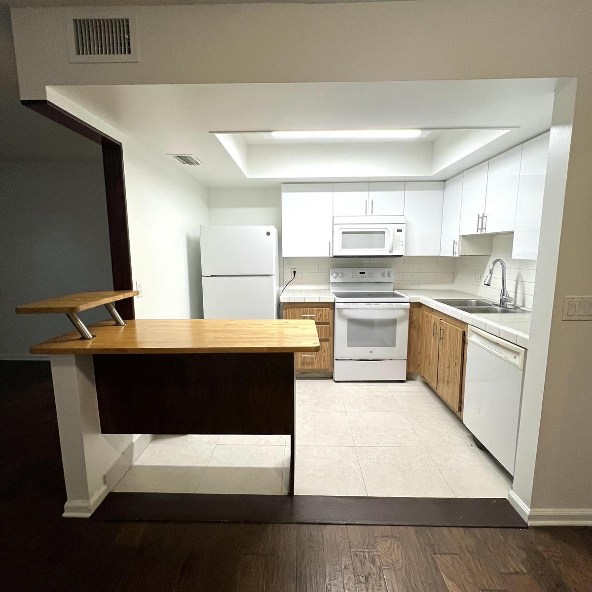 A kitchen with white upper cabinets, wood lower cabinets, white appliances, and a breakfast bar — 4205 Oak Terrace Drive # 4205, FL 33463, FL