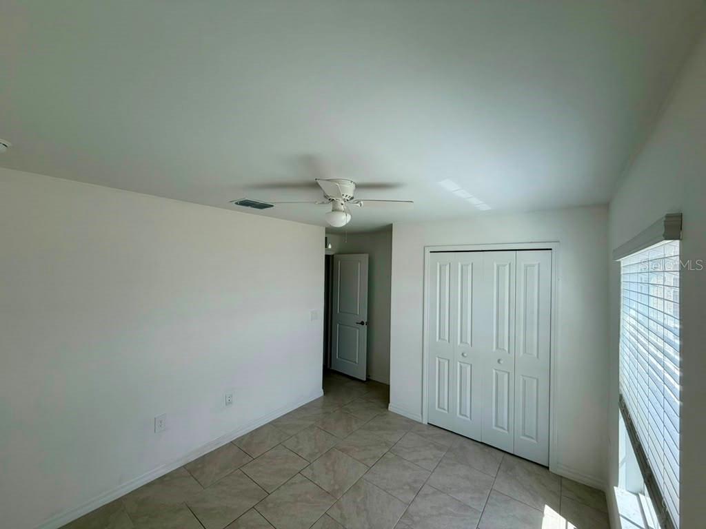 A bedroom with tile flooring, a ceiling fan, a closet, and an open doorway — 4104 NE 12TH COURT, CAPE CORAL, FL