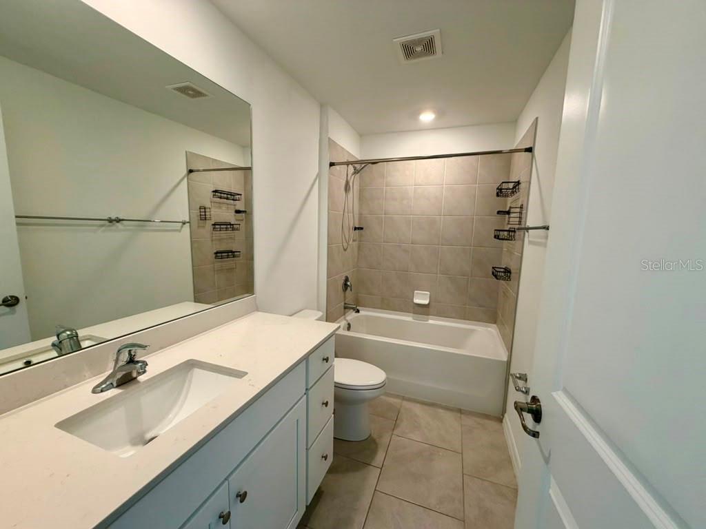 A bathroom features a white vanity, a tiled tub-shower combination, and light-colored floor tiles — 4104 NE 12TH COURT, CAPE CORAL, FL