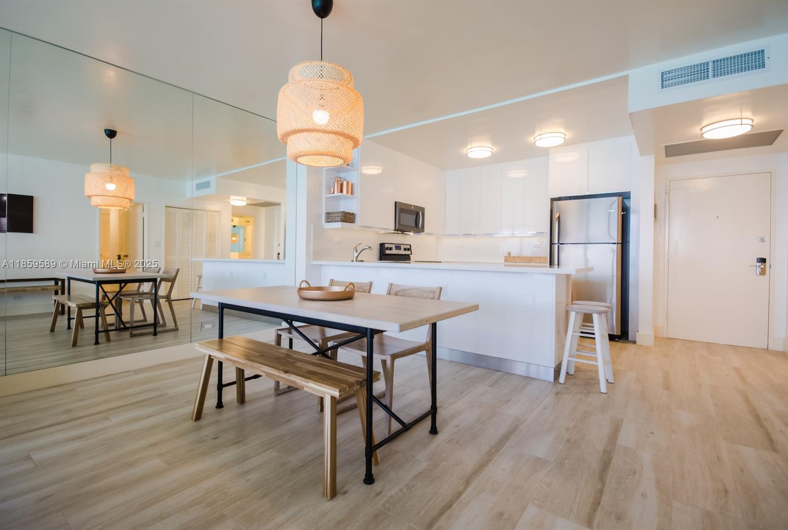 A dining area with a wooden table and bench sits before a modern white kitchen — 5601 Collins Ave # 1204, Miami Beach FL 33140, MIAMI BEACH, FL