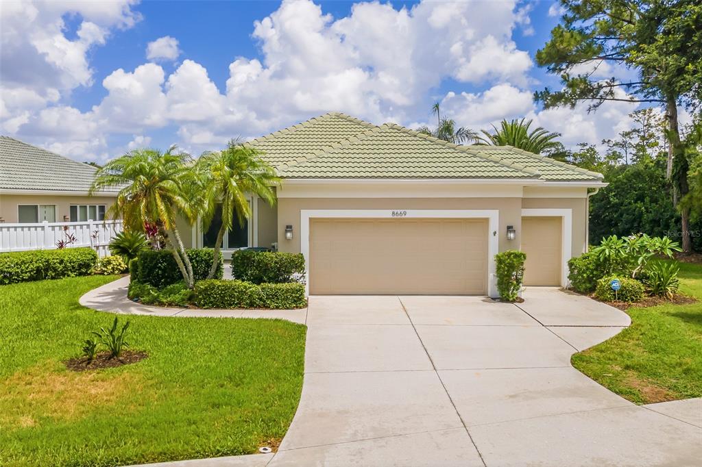 A tan single-story house with a green tile roof and a two-car garage — 8669 54TH AVENUE CIRCLE E, BRADENTON, FL