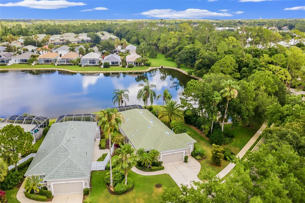 An aerial view shows two suburban homes with green roofs situated beside a large pond — 8669 54TH AVENUE CIRCLE E, BRADENTON, FL