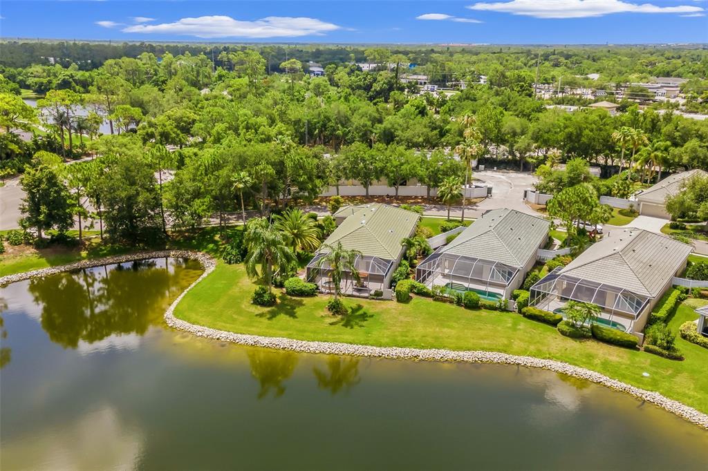 An aerial view shows three houses with screened-in pools situated along a pond — 8669 54TH AVENUE CIRCLE E, BRADENTON, FL