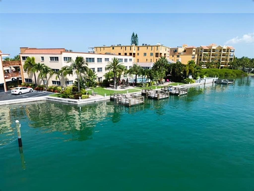An aerial view shows a multi-story apartment complex situated along a waterfront with private docks — 10265 GULF BOULEVARD UNIT A308, ST PETERSBURG, FL