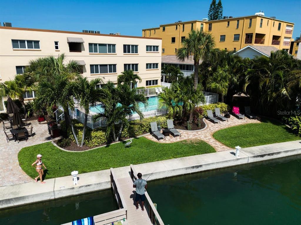 An aerial view shows a swimming pool area with lounge chairs, palm trees, and a canal — 10265 GULF BOULEVARD UNIT A308, ST PETERSBURG, FL