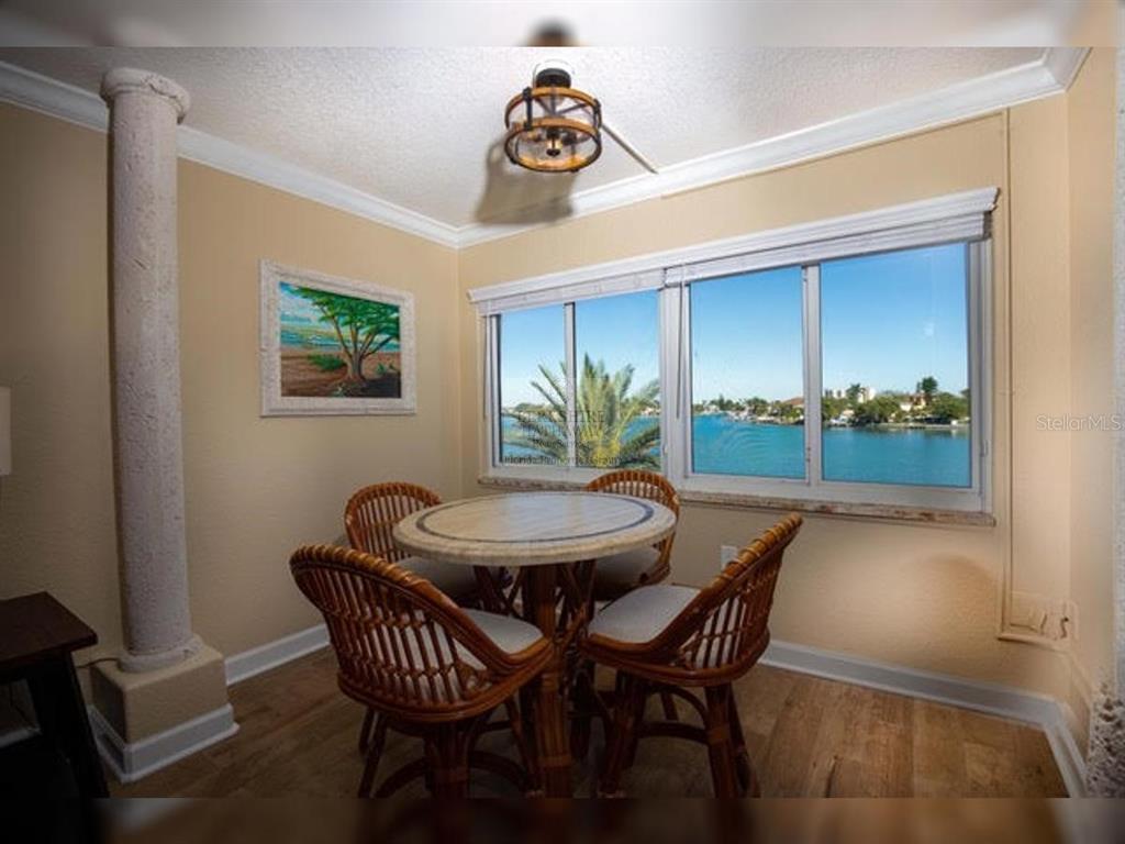 A dining area features a round stone table, wicker chairs, and a waterfront window view — 10265 GULF BOULEVARD UNIT A308, ST PETERSBURG, FL